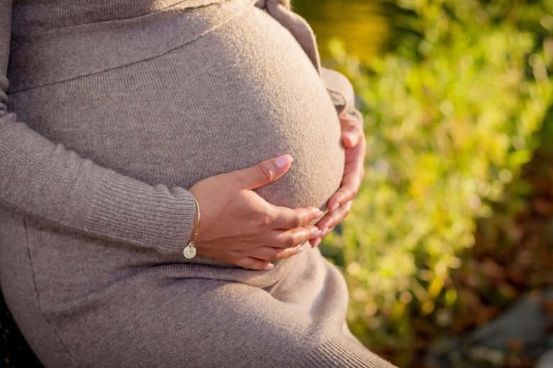 pregnant woman wearing gray long-sleeved dress touching her tummy while standing